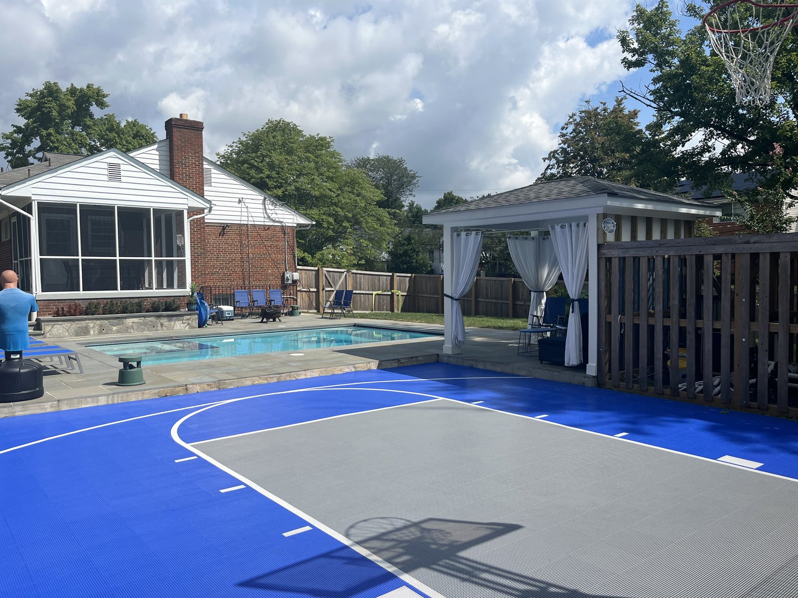 A finished blue and grey backyard basketball court beside a pool, built with Outdoor Sport Courts interlocking tiles